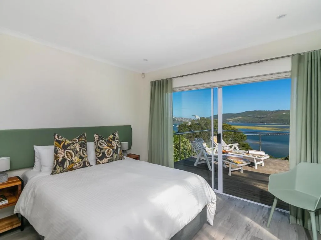 Spacious bedroom with bed, green headboard, and lagoon views through glass doors