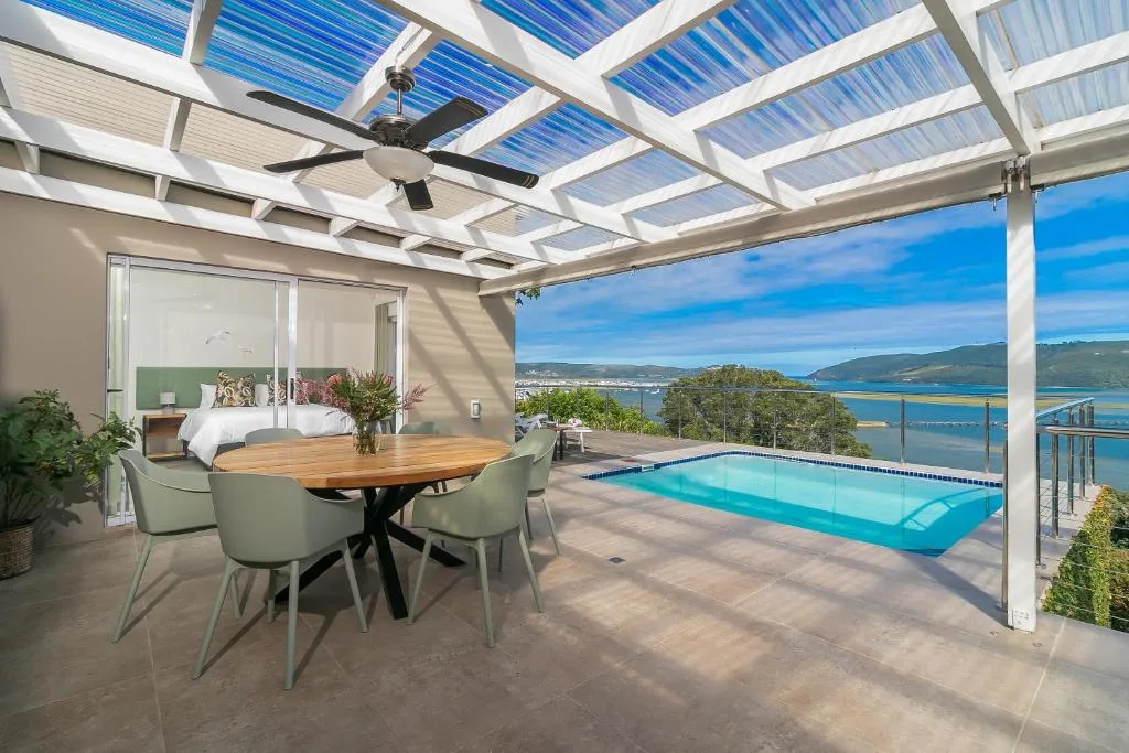 Covered patio with dining table, pool, and Knysna lagoon views