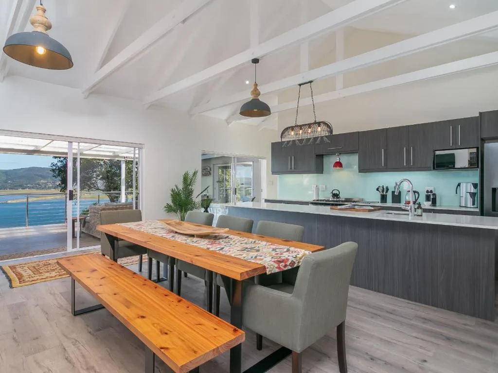 Modern dining area with wooden table, bench seating, and ocean view through glass doors