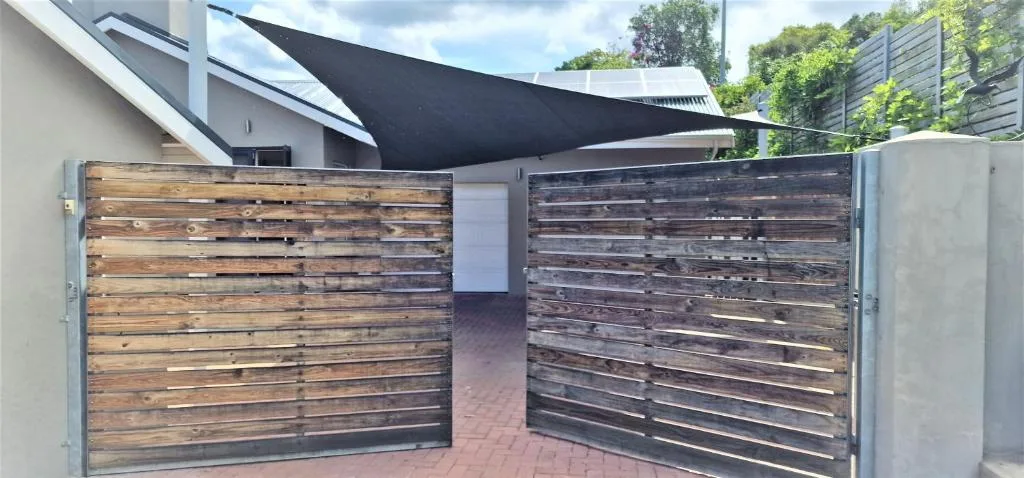 Modern villa entrance with wooden gates and black shade sail