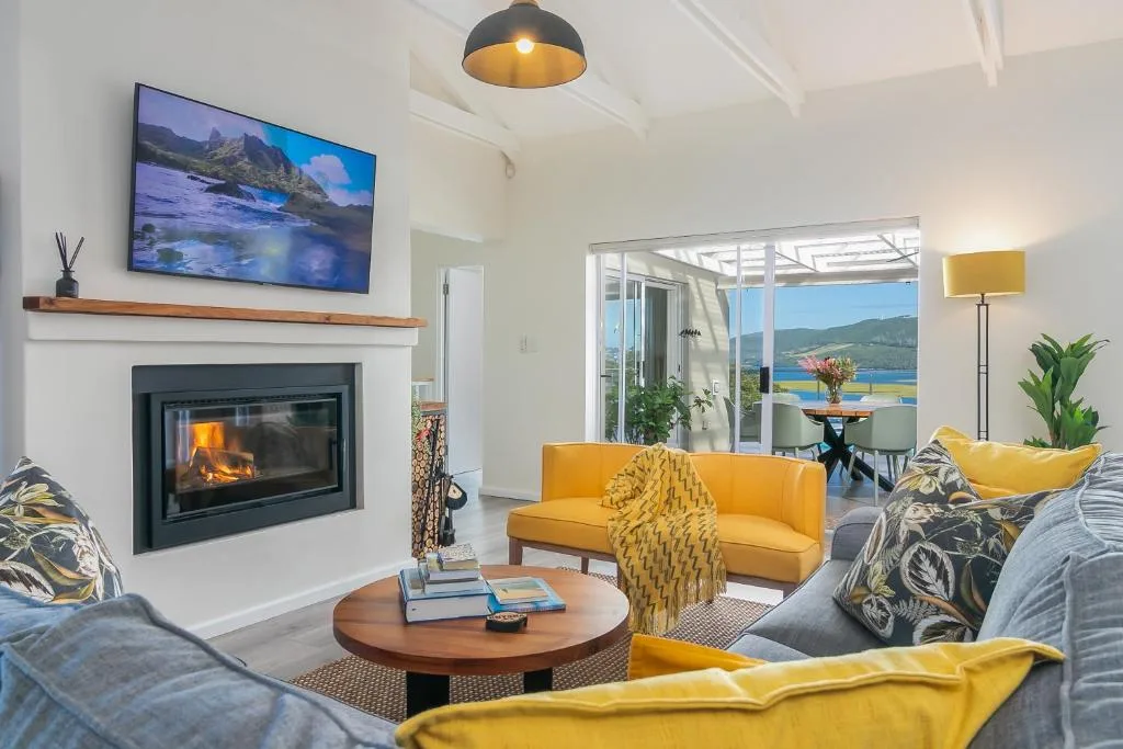Bright lounge with fireplace, yellow sofa, and lagoon views through glass doors