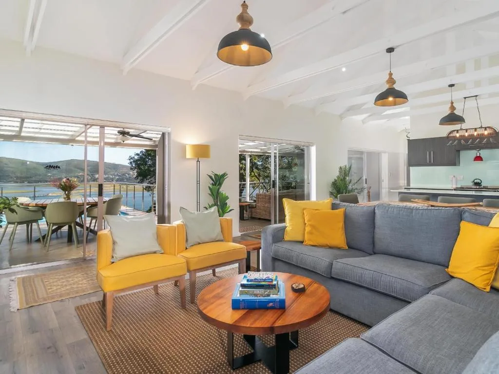 Modern lounge with gray sofa, yellow armchair, and water views through glass doors