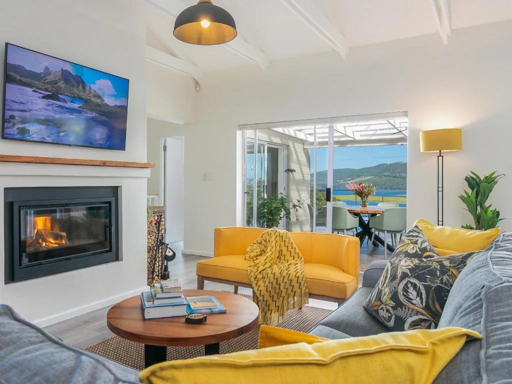 Modern lounge with fireplace, yellow sofa, and lagoon views through glass doors