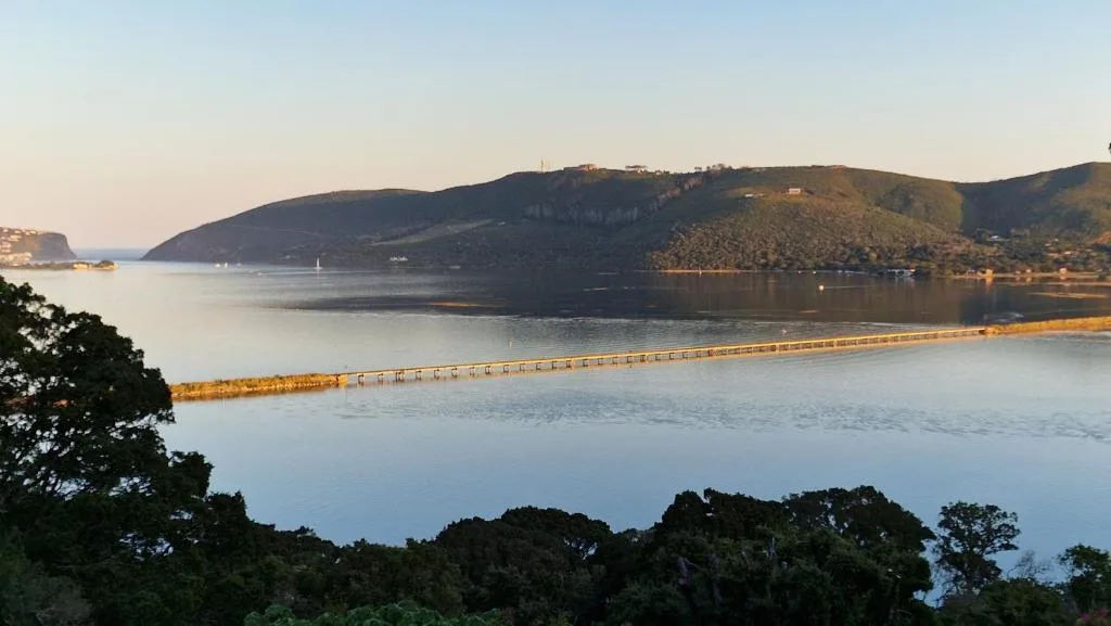 Serene lagoon view with wooden pier, forested hills, and calm water at sunrise