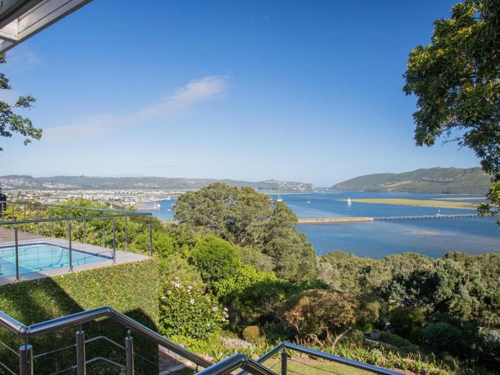 Panoramic Knysna Lagoon vista with sailboats, lush hillside gardens, and pool