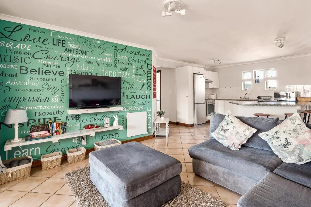 Open-plan lounge with grey sofa, inspirational wall art, and TV entertainment area