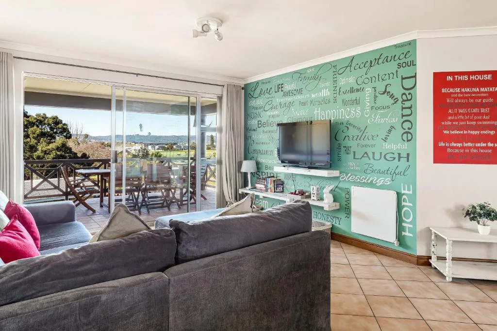 Open-plan lounge with gray sofa, inspirational wall art, and sliding doors to deck