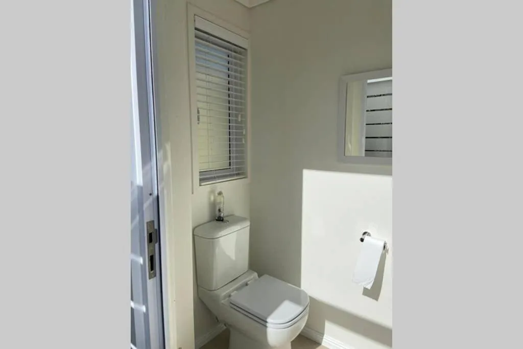 Clean bathroom with toilet, sink, and louvered window for ventilation