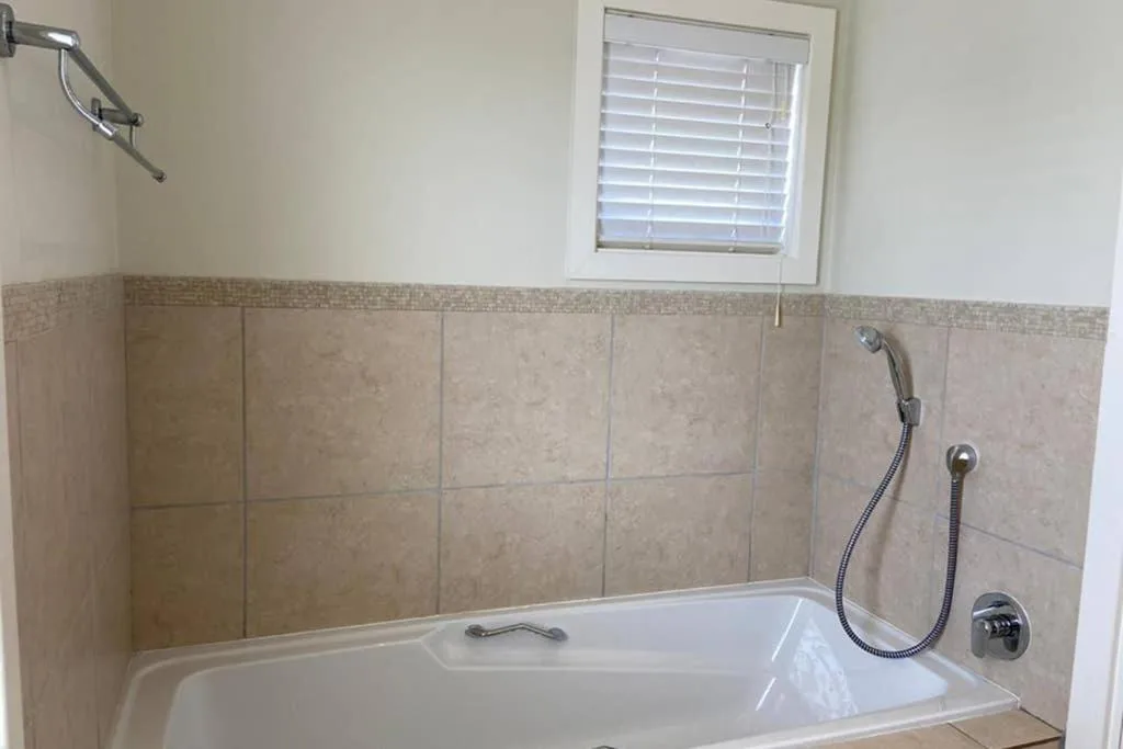 Clean bathroom with bathtub, beige tile walls, and window with blinds