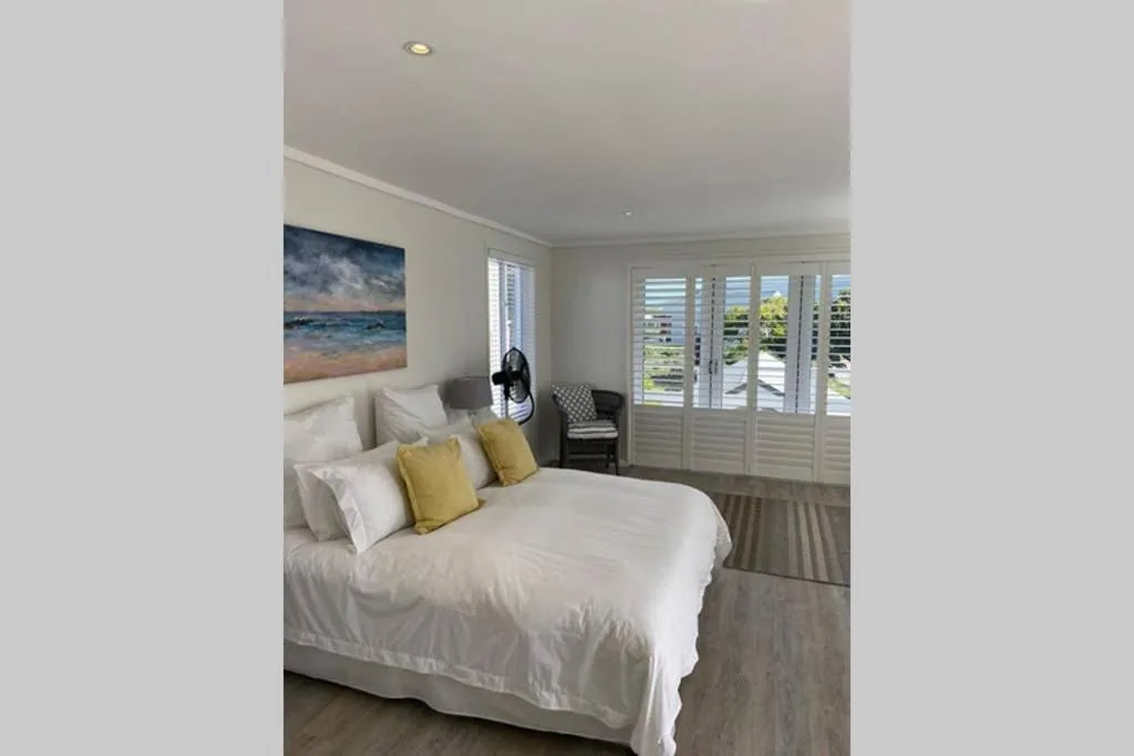 Bright bedroom with queen bed, yellow pillows, ocean artwork, and louvered doors