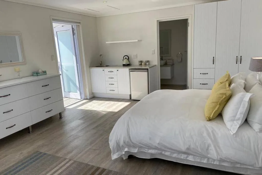 Spacious bedroom with white bedding, yellow accent pillow, modern furniture, and ensuite bathroom access