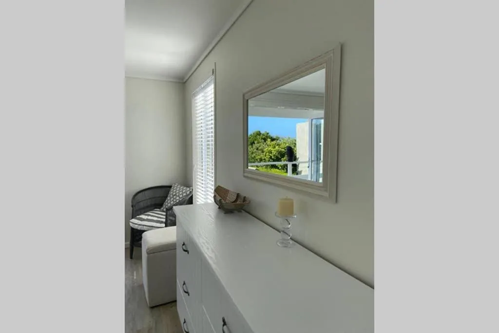 Bright bedroom with white dresser, mirror, and garden view through window