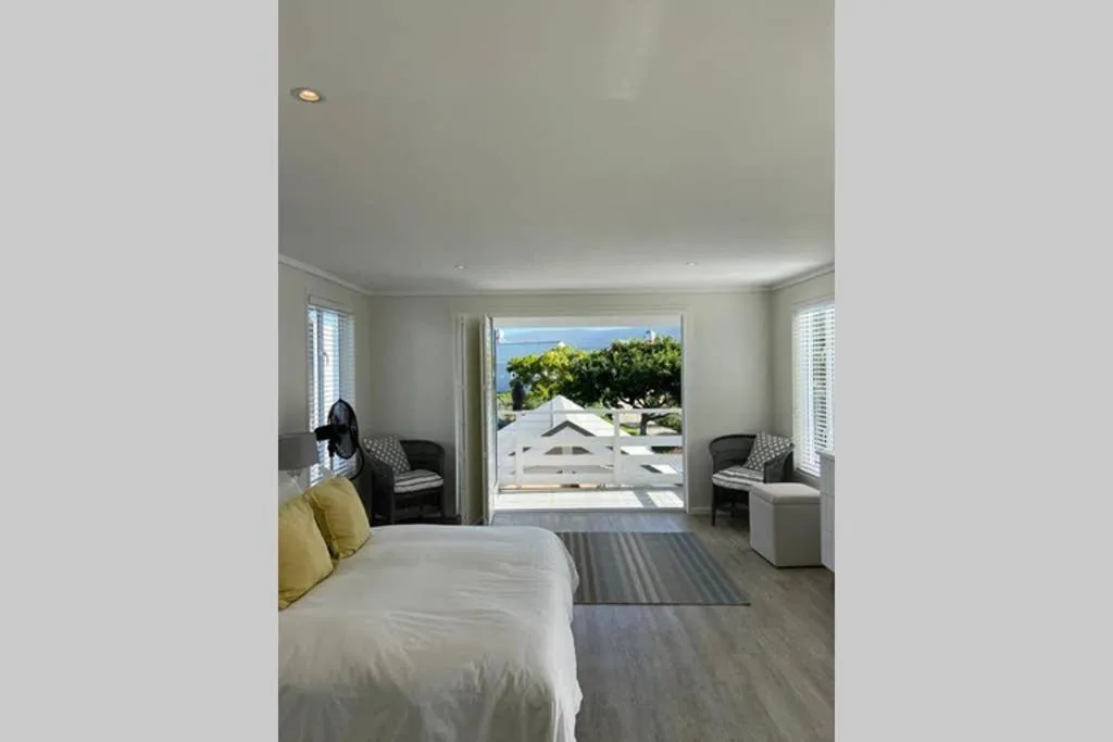 Bright bedroom with white bed, yellow accent pillow, and ocean view through glass doors