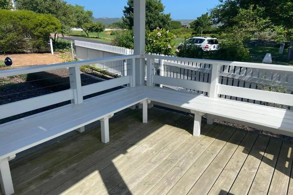 Spacious wooden deck with white railings and built-in seating overlooking gardens