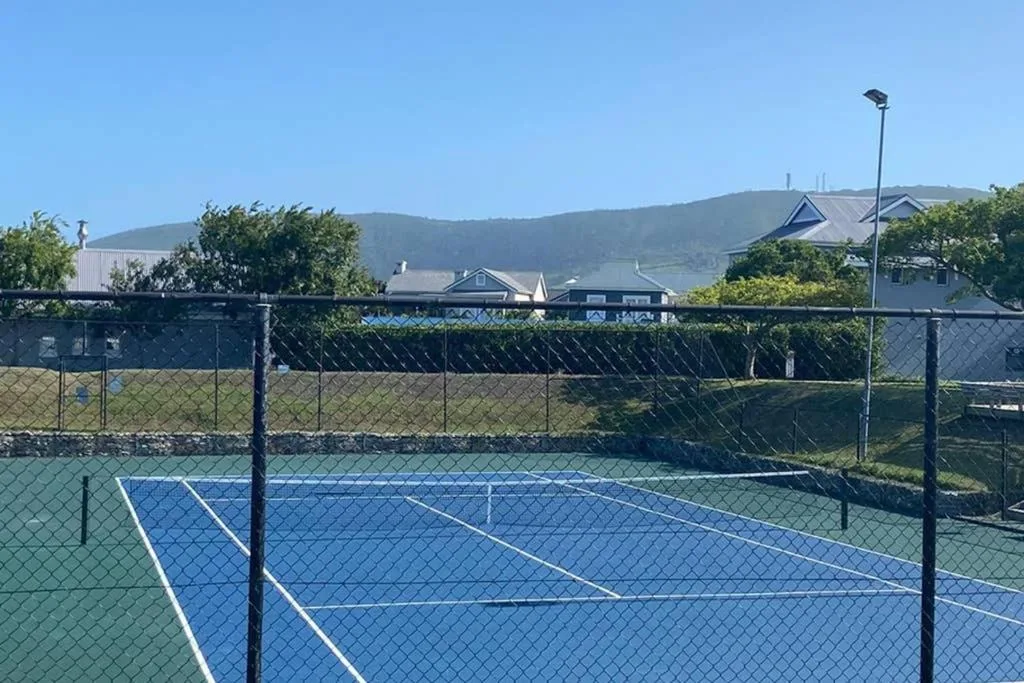 Tennis court with blue surface and mountain views beyond fenced enclosure