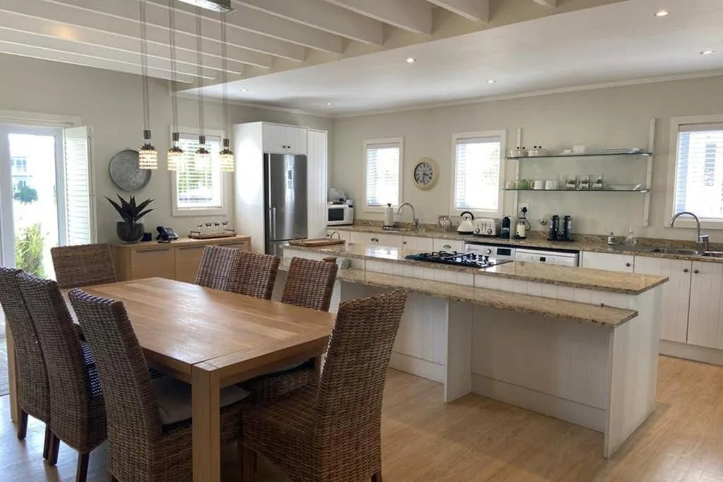 Open-plan dining area with wooden table and wicker chairs overlooking kitchen