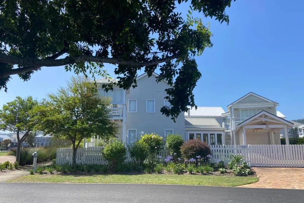 Light blue cottage with white picket fence and manicured garden on sunny day