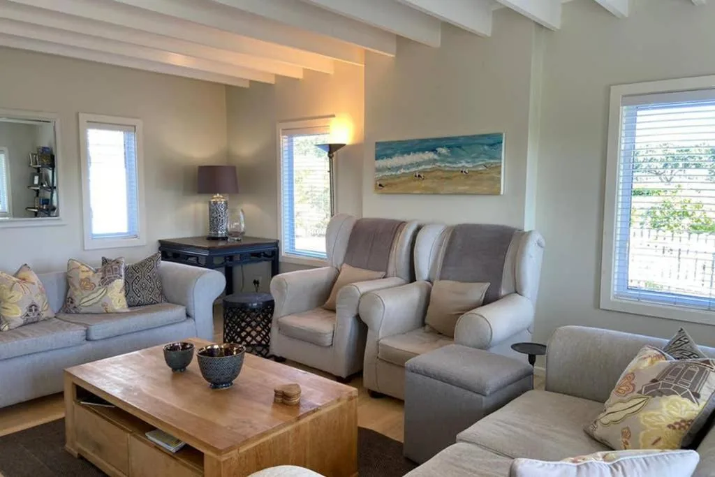 Bright living room with cream armchairs, sofa, wooden coffee table, and coastal artwork