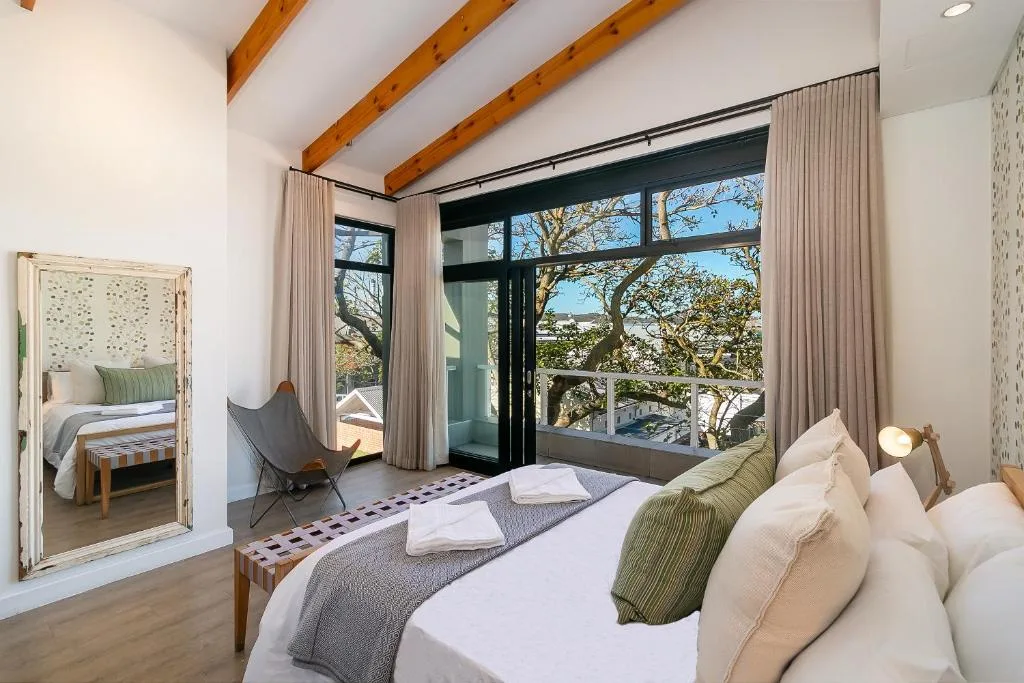 Spacious bedroom with double bed, exposed wooden beams, and large glass doors overlooking trees