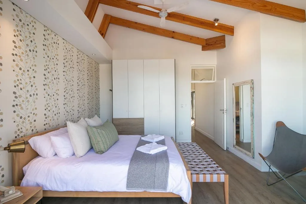 Bright bedroom with double bed, patterned wallpaper, wooden beams, and ensuite access