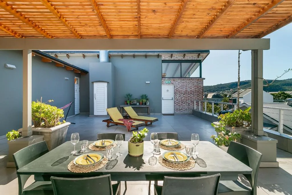 Covered rooftop deck with dining table and lounge chairs overlooking green hills