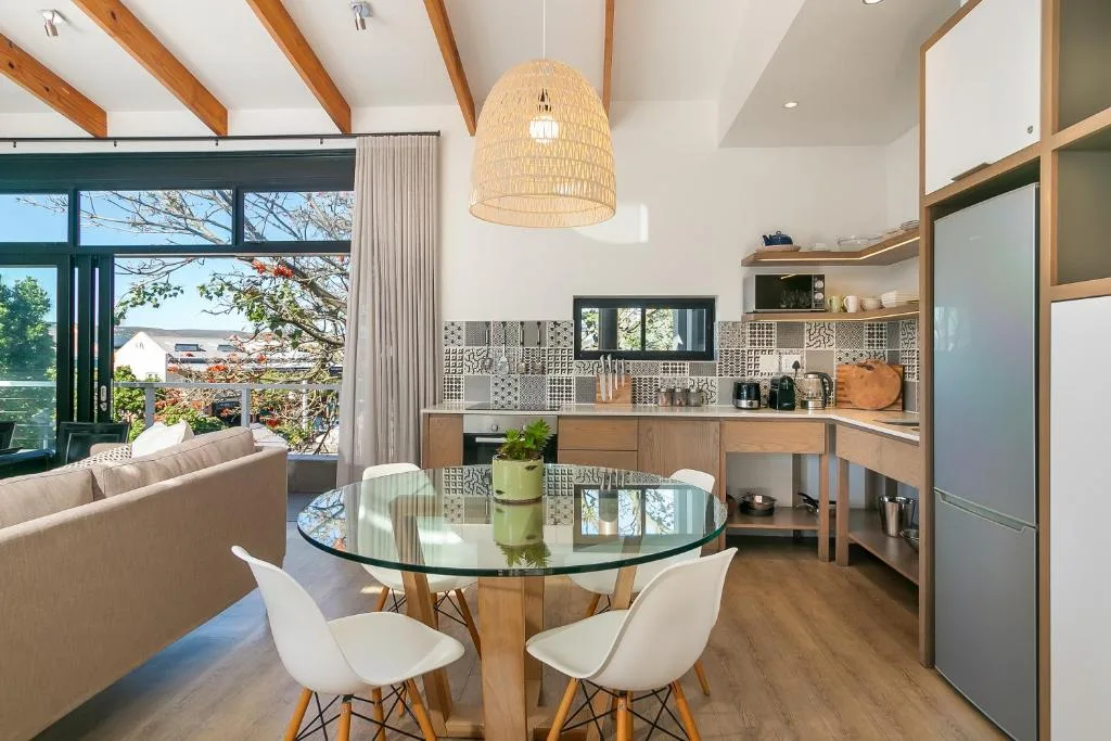 Open-plan lounge with dining table and kitchen area, exposed wooden beams