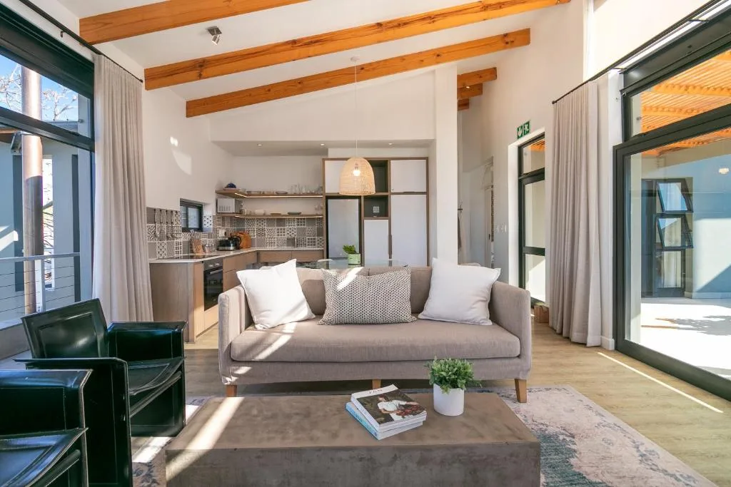 Bright open-plan lounge with grey sofa, wooden beams, and glass doors