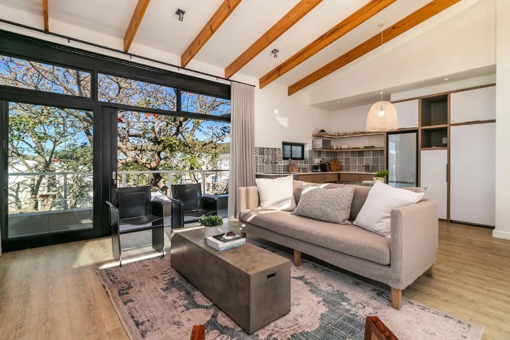 Modern living room with cream sofa, exposed wooden beams, and large windows overlooking trees