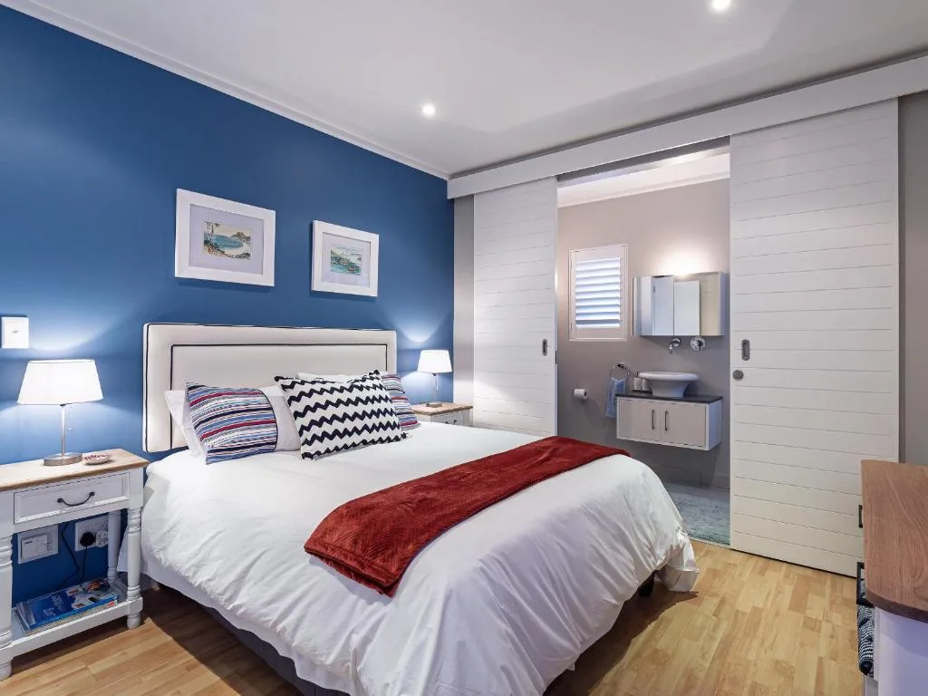 Modern bedroom with blue accent wall, white bedding, and en-suite bathroom visible
