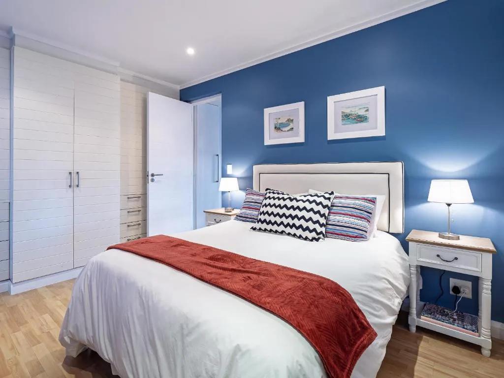Modern bedroom with blue walls, queen bed, white bedding, and coastal artwork