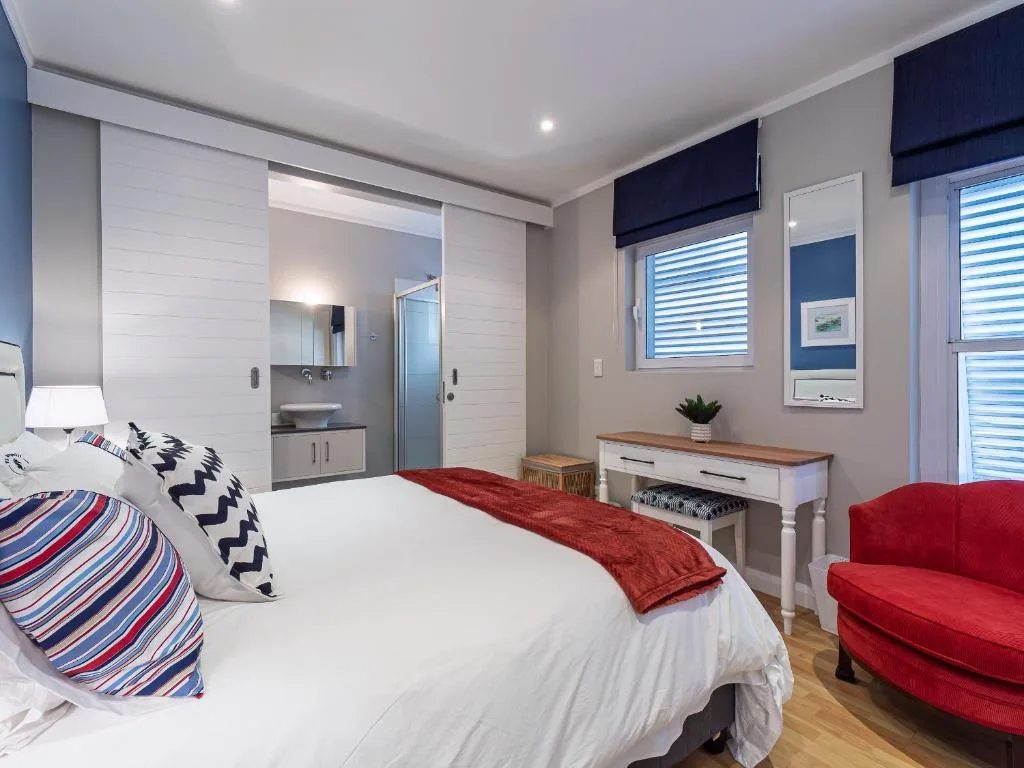 Modern bedroom with queen bed, red armchair, and ensuite bathroom visible