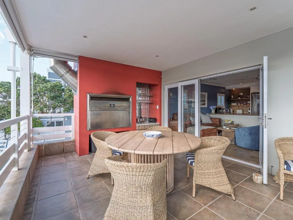 Modern covered deck with round dining table and woven chairs overlooking lagoon