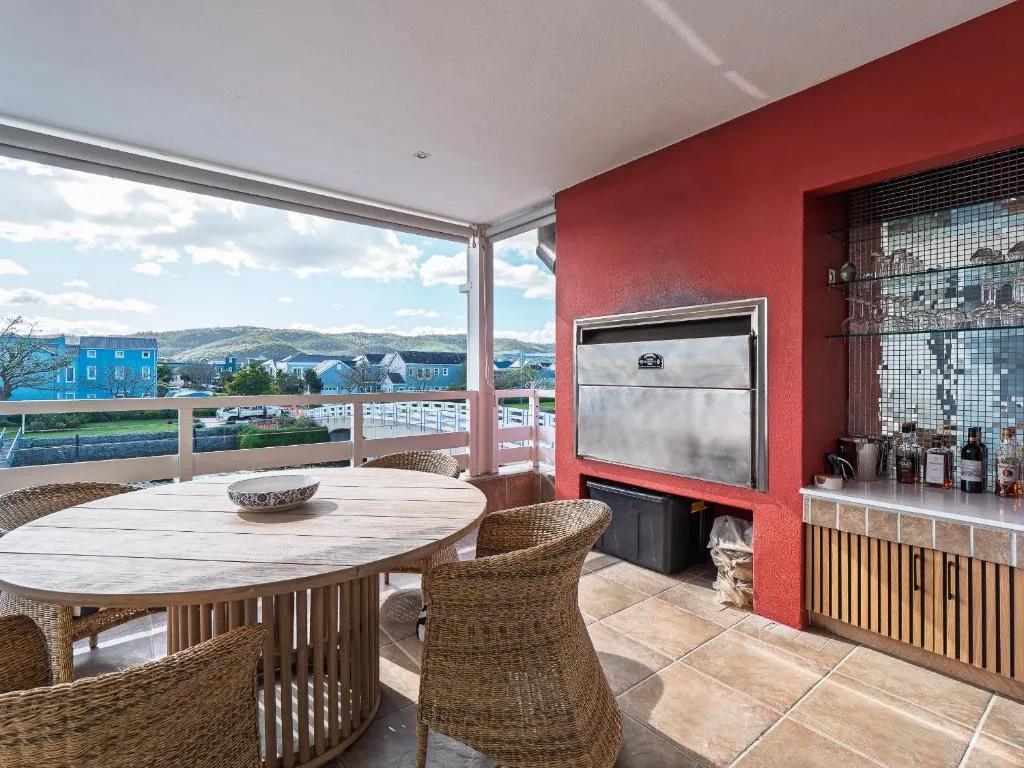 Covered outdoor patio with dining table, chairs, and braai area overlooking Knysna