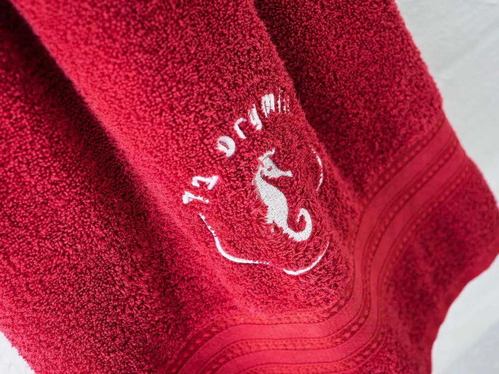 Close-up of branded red towel with embroidered seahorse logo detail