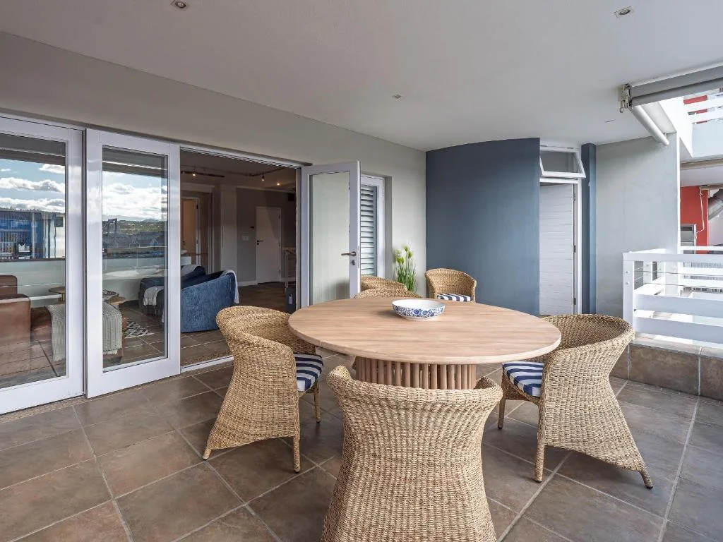 Modern dining area with round wooden table and woven chairs overlooking garden route