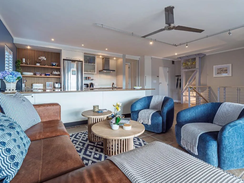 Modern living room with blue armchairs, leather ottoman, and open-plan kitchen