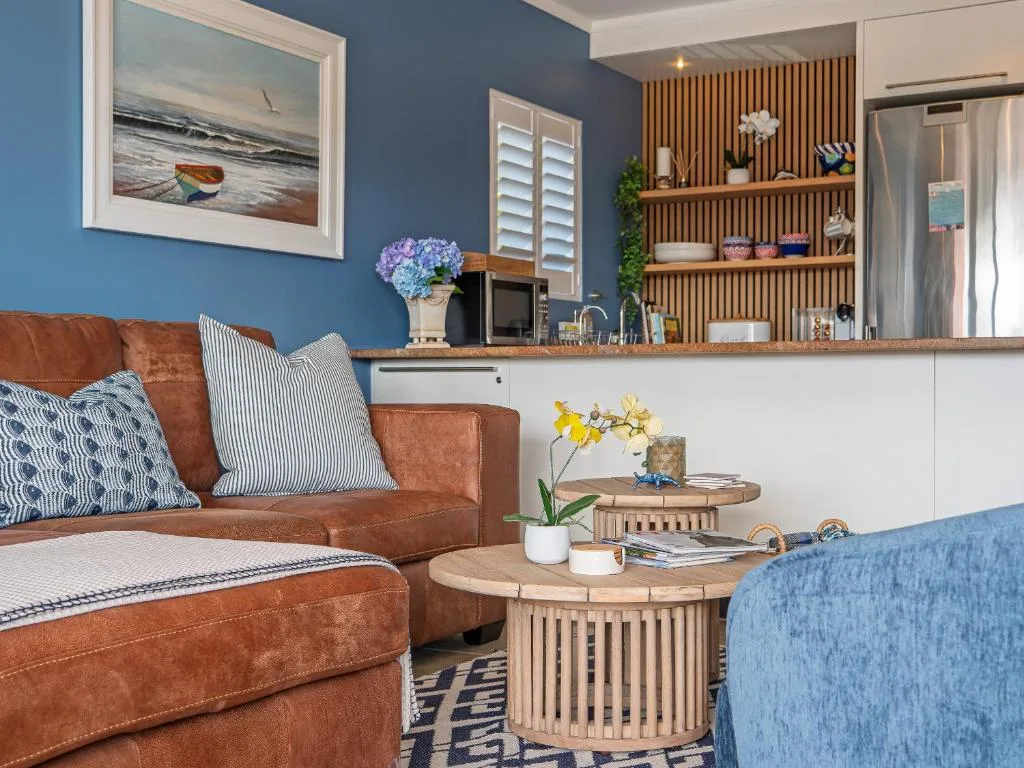 Contemporary lounge with cognac leather sofa, blue accent chair, and open kitchen.