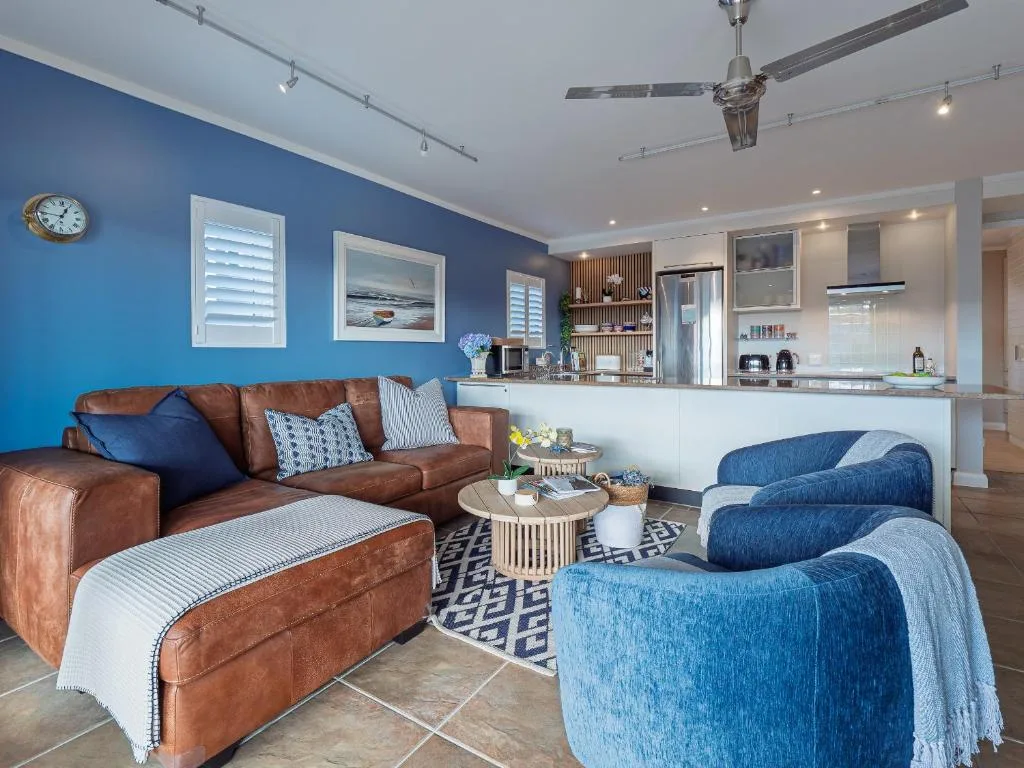 Open-plan lounge with brown leather sofa and blue armchairs, kitchen beyond