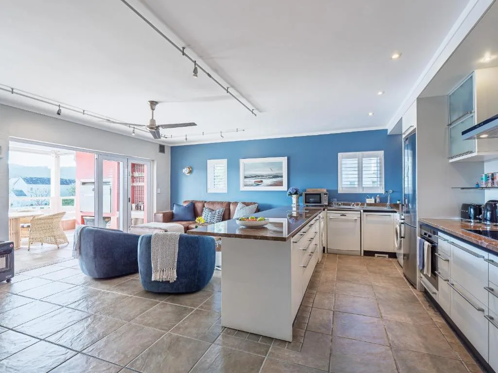 Modern lounge with blue accent wall, sofa, and open-plan kitchen area