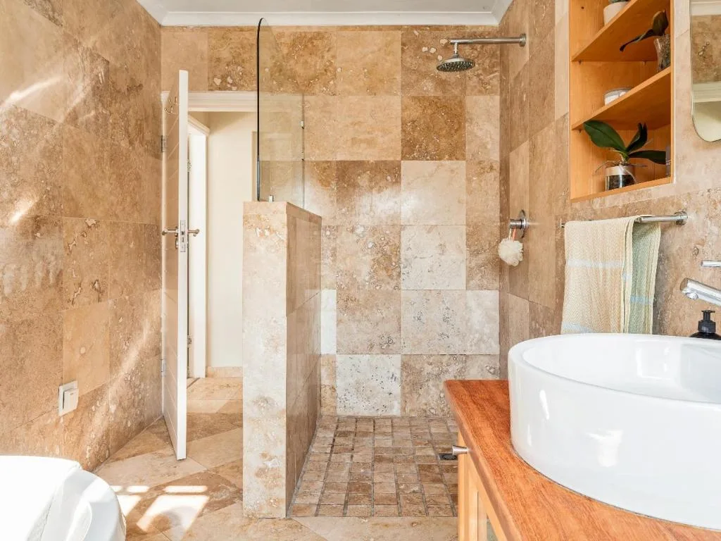 Modern bathroom with travertine tiles, rainfall shower, and round vessel sink