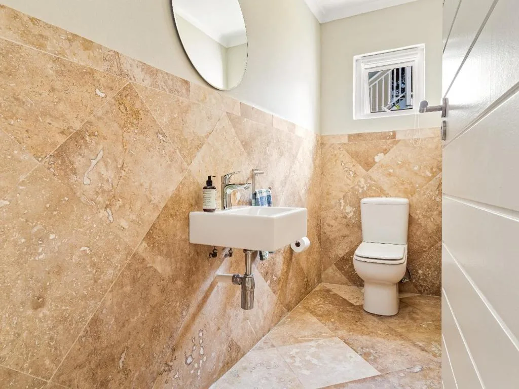 Modern bathroom with travertine tile walls, white sink, and toilet