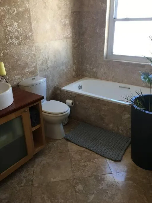 Bathroom with white bathtub, toilet, and natural light from window