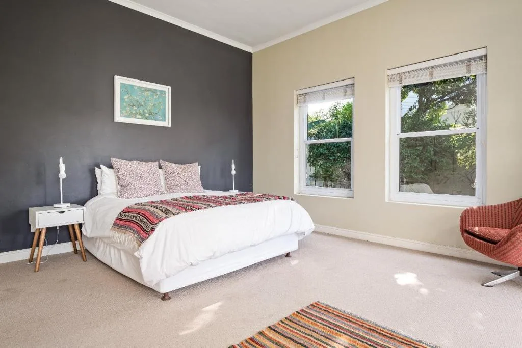Bright bedroom with queen bed, dark accent wall, large windows overlooking garden