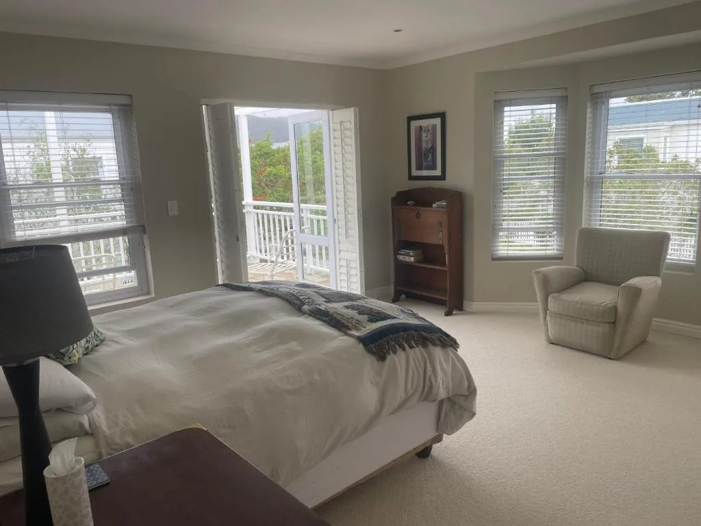 Bright master bedroom with queen bed, armchair, and multiple windows overlooking garden