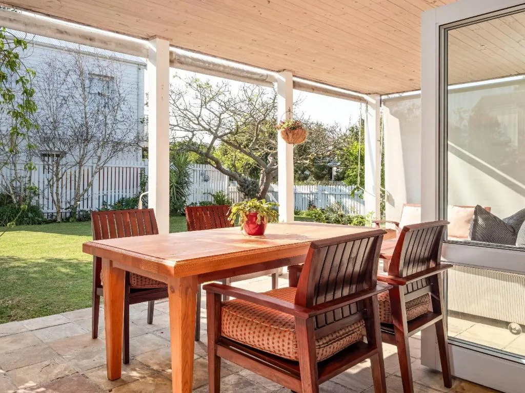 Covered patio with wooden dining table and chairs overlooking green garden
