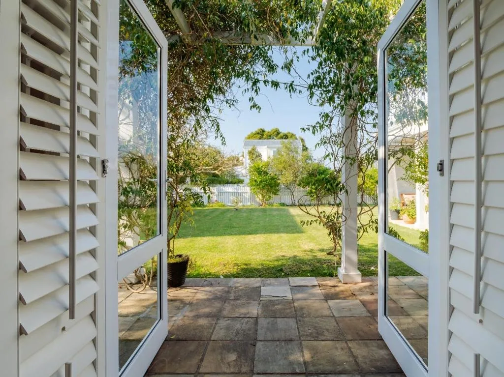 Open glass doors leading to paved patio and manicured garden lawn