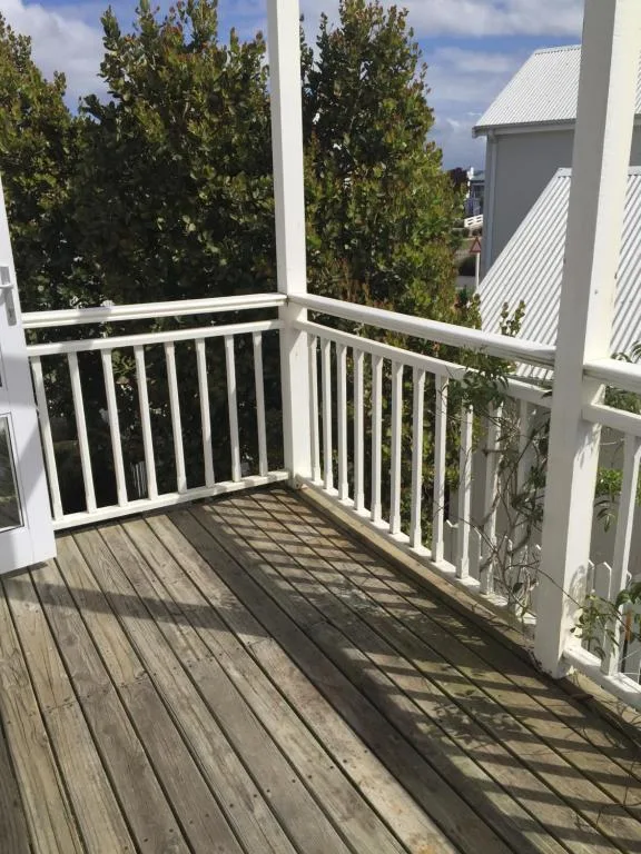 Wooden deck with white railings overlooking trees and garden