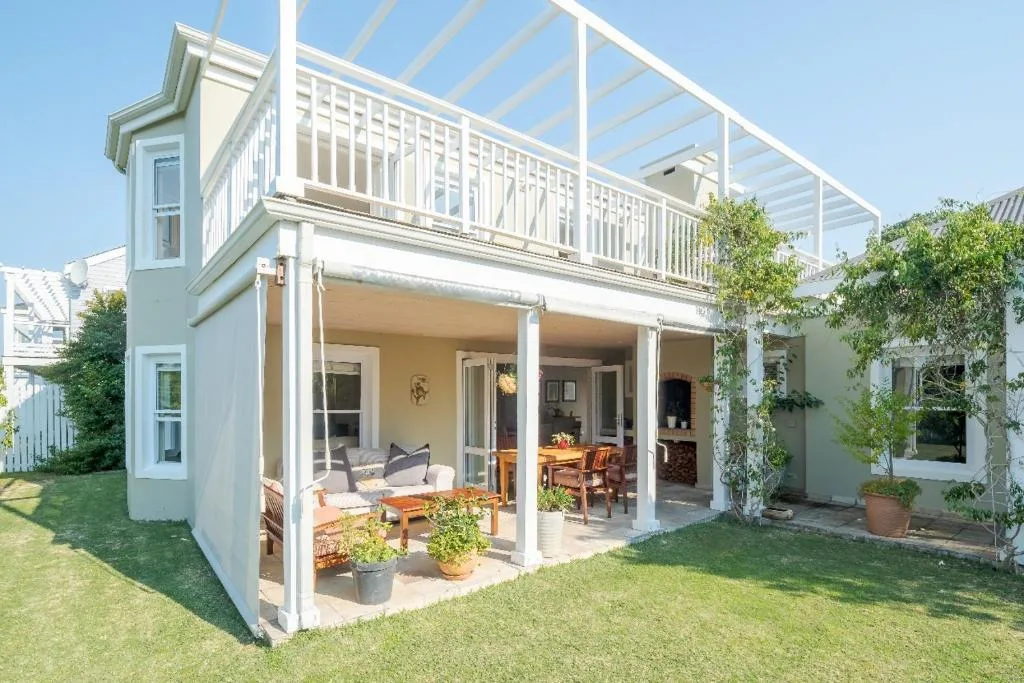White cottage with upper deck, covered porch, and manicured lawn