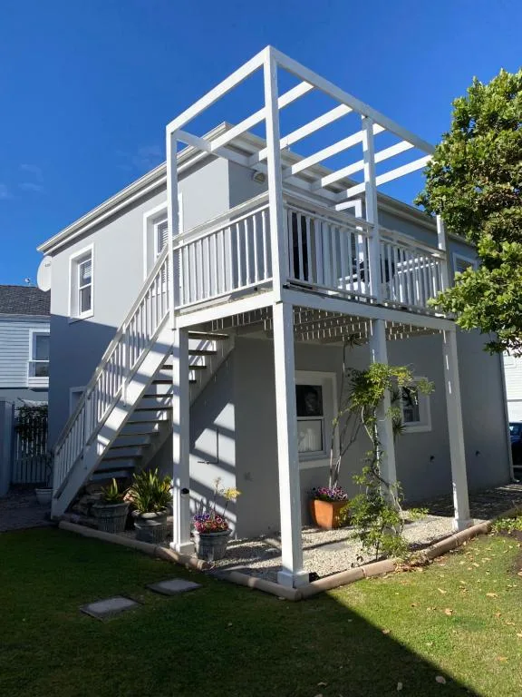 Modern white cottage with elevated deck and wooden pergola, garden entrance
