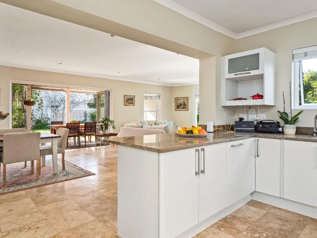 Modern white kitchen with granite countertop island, open to lounge and deck beyond